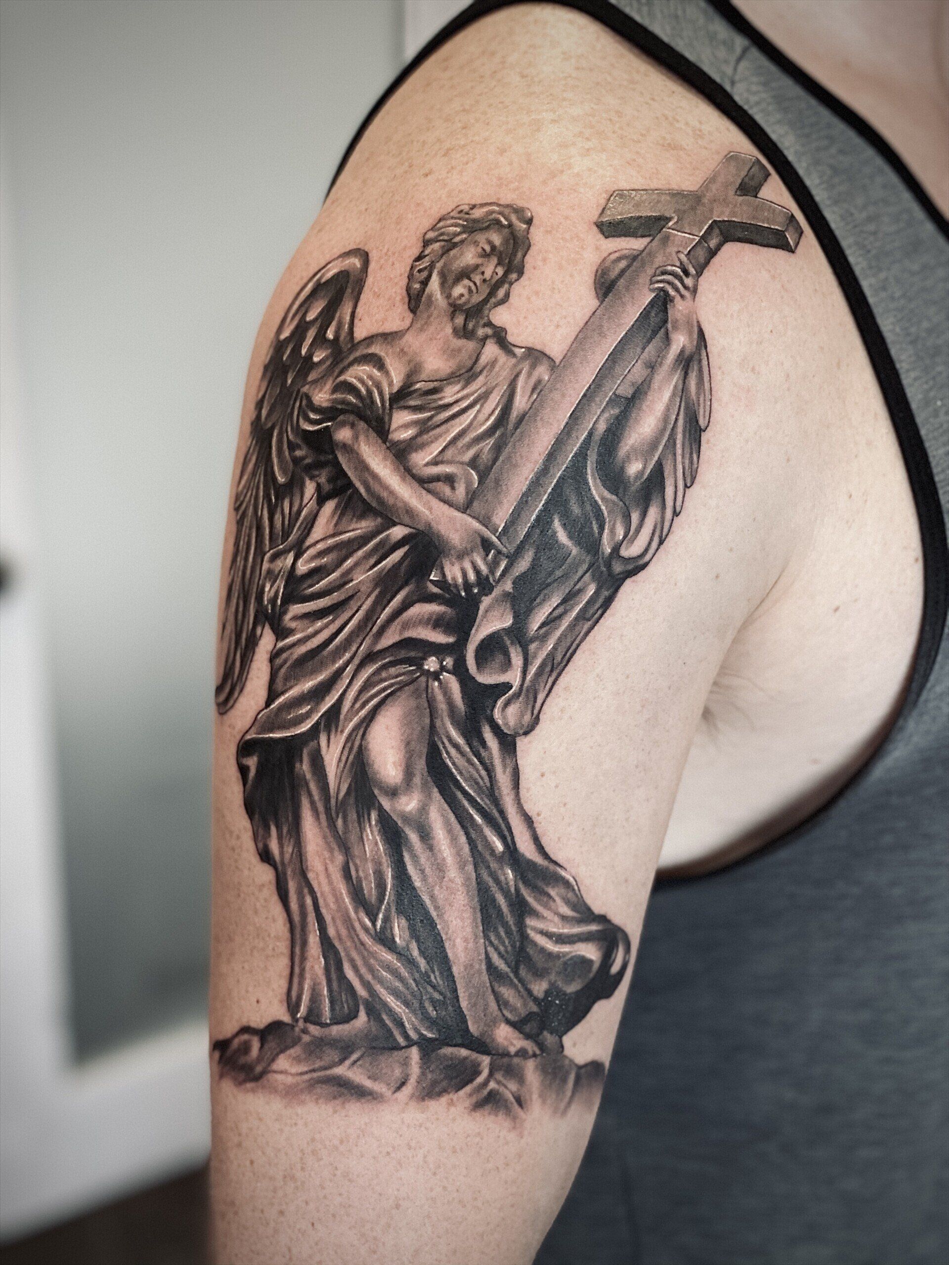 A man has a tattoo of an angel holding a cross on his arm